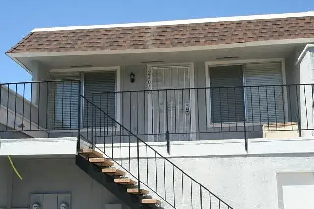 Two-story apartment with brown roof, outdoor staircase, and front railing.