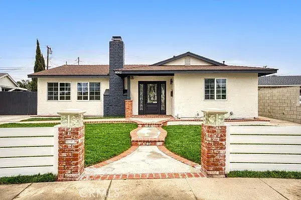 Single-story cream house with chimney, lawn, brick path, and white fence.