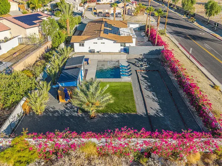 Aerial view of backyard with pool, lounge chairs, lawn, palm trees, and flowering shrubs.