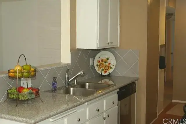 Kitchen with white cabinets, gray countertop, dual sink, and fruit basket.