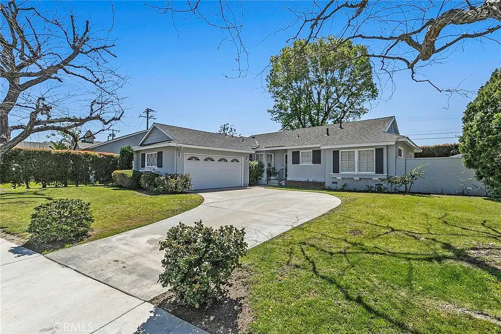 Single-story gray house with two-car garage, curved driveway, hedges, and green lawn.