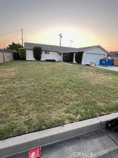 Single-story white house with two-car garage, green lawn, and sunset sky.