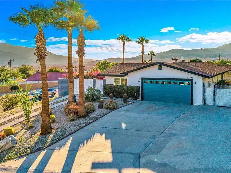 Single-story house with blue garage door, palm trees, and mountain views.