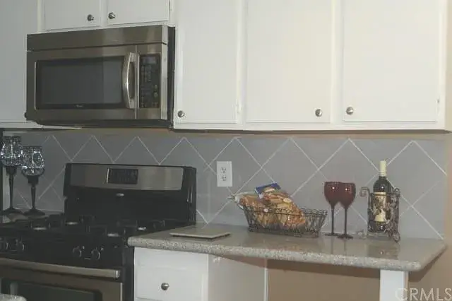 White kitchen with stainless steel appliances, gray backsplash, wine glasses, and snack basket.