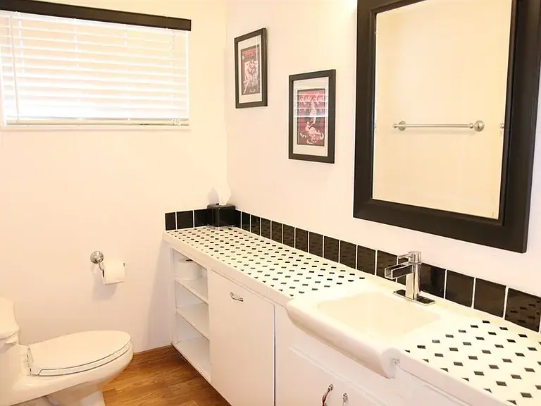 Bright bathroom with sink, black-framed mirror, toilet, and patterned tile countertop.