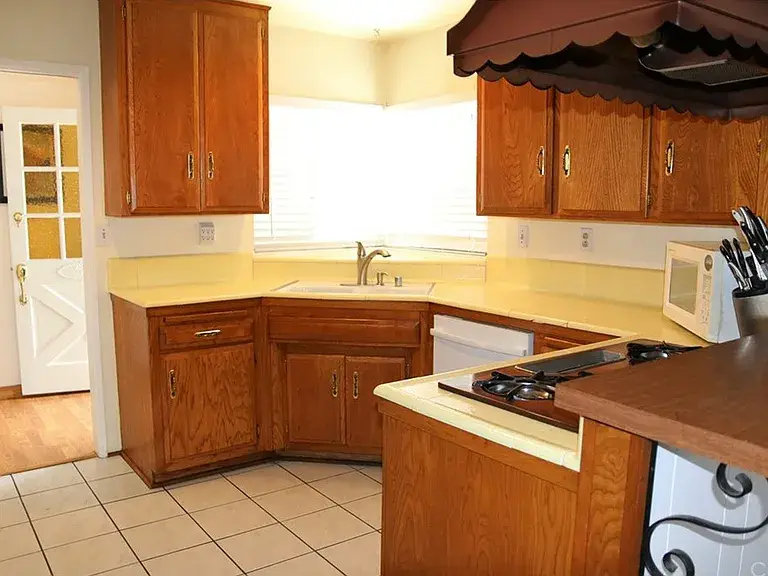 Cozy kitchen with oak cabinets, yellow countertops, corner sink, and tiled floor.