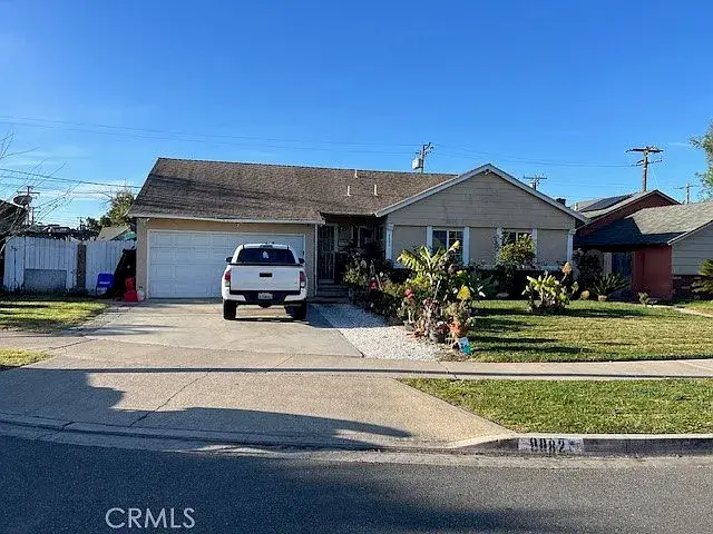 Single-story beige house with shingle roof, driveway, and front garden under a blue sky.