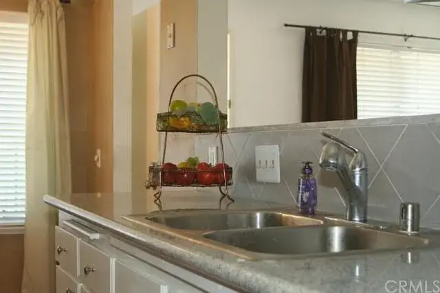 Modern kitchen sink area with double basin, silver faucet, and fruit basket.